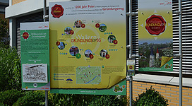 Ein Informationsschild über den Gründungsweg mit einer Karte und historischen Bildern. Es feiert das 1200-jährige Bestehen.