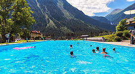 Ein schöner Swimmingpool inmitten der Berge. Menschen schwimmen und entspannen sich im klaren blauen Wasser.