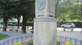 Billroth - Denkmal in St. Gilgen: Das Bild zeigt einen Gedenkstein in einer stimmungsvollen Parkanlage. Der Stein ist aus Stein gefertigt und trägt eine metallische Plakette. Um den Stein herum erstrecken sich gepflegte Blumenbeete mit einer Vielzahl an bunten Blüten.