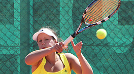 Union Tennis Club Fischer Ried in Ried im Innkreis: Eine Person in einem gelben Trikot spielt Tennis auf einem Tennisplatz. Sie hält einen Tennisschläger und blickt konzentriert auf einen gelben Tennisball, der auf sie zufliegt.