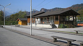 Ein Gebäude mit einem angegliederten Außenbereich in einer ländlichen Umgebung. Im Hintergrund sind Berge und ein klarer Himmel sichtbar.