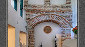 Museum Alte Stadtmauer und Schmiedemuseum in Vöcklabruck: Eine alte Gebäudefront mit Bögen und Ornamenten an der Fassade. Es sieht aus wie ein Eingang oder eine Pforte. Im Vordergrund ist ein Platz mit Pflastersteinen und einigen Möbeln oder Dekorationen.