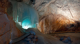 Eine beeindruckende Eishöhle mit blauen Lichtern und vereisten Felsen. Der Weg führt in einen geheimnisvollen Raum hinter dem Eis.