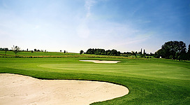 Golfclub Schärding/Maad in Taufkirchen an der Pram: Eine weitläufige Golfplatzlandschaft erstreckt sich unter einem strahlend blauen Himmel. Der Rasen ist makellos grün, durchzogen von hell schimmernden Sandbunkern. Einzelne Bäume säumen den Platz und verleihen dem Gelände eine angenehme, natürliche Atmosphäre.
