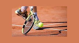 Spielszene mit Tennisball und Schläger auf einem roten Sandplatz im Freien
