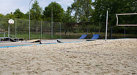 Beach-Volleyball Platz Nußdorf in Nußdorf am Attersee: Das Bild zeigt einen Outdoor-Sportplatz mit einer Basketballanlage, Rampen und Sandplätzen. Die grüne, waldige Umgebung mit Bäumen und Sträuchern bietet eine angenehme Kulisse für diese Freizeiteinrichtung.
