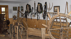 Heimathaus Weng in Weng im Innkreis: Ein Raum mit zahlreichen Holzmöbeln und an den Wänden hängenden Objekten, die an traditionelle ländliche Dekorationen erinnern. Verschiedene Holzstühle und -tische sind in dem Raum angeordnet, der den Eindruck eines gemütlichen Ambiente vermittelt.