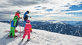 Eine Gruppe von Skifahrern steht auf einem verschneiten Berggipfel. Die Aussicht auf die umliegenden Berge ist atemberaubend.