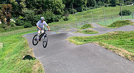 Männlicher Biker fährt den Rundparcours und springt über eine Welle des Pumptracks.