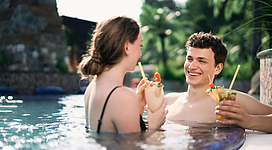 Ein Paar entspannt im Schwimmbecken und genießt farbenfrohe Cocktails. Die Atmosphäre ist freundlich und romantisch.
