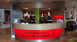 Ein Empfangstresen in einem modernen Fitnessstudio. Die beleuchtete Anzeige vermittelt eine motivierende Botschaft für die Besucher.