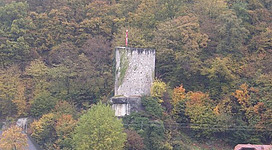 Rundturm Sarmingstein in St. Nikola an der Donau: Eine imposante Burg thront auf einem Felsen, umgeben von einem bunten Herbstlaub. Die Burg ist von einer massiven Steinmauer umgeben und verfügt über einen hohen Turm. Das Gebäude ist in traditioneller Architektur gehalten und scheint ein historisches Bauwerk zu sein. Die malerische Landschaft mit den umliegenden Wäldern und Bergen komplettiert das idyllische Bild.