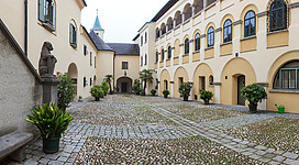 Ein malerischer Innenhof mit gepflastertem Boden und Pflanzen. Die umstehenden Gebäude haben einen historischen Charme und schöne Fenster.