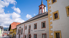 Ein malerischer Straßenblick mit historischen Gebäuden und einer Kirche im Hintergrund. Der Himmel ist blau mit einigen Wolken.