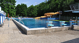 Ein Schwimmbad mit klarem Wasser und einer Rutsche im Hintergrund. Die Umgebung ist grün und einladend, ideal für einen erfrischenden Sommertag.