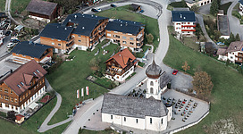 Luftbild der Kath. Pfarrkirche hl. Josef mit Friedhof und Umgebung in Bürserberg.