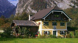 Ein charmantes, gelbes Haus mit einem Garten, umgeben von wunderschönen Bergen. Die Vorderansicht zeigt Holzfenster und blühende Pflanzen.
