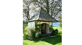Blick auf die Kapelle, im Hintergrund Bäume, im Vordergrund Wiesen, Sträucher
