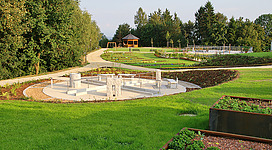 Kneipp Garten in Bad Kreuzen: Ein gepflegter Garten mit kunstvoll angelegten Beeten, Wegen und einem Pavillon. Inmitten einer grünen Landschaft mit Bäumen und Sträuchern befinden sich verschiedene Erholungsmöglichkeiten wie Spielgeräte und Rastplätze.