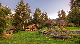 Rekonstruierte keltische Hütten mit Strohdächern inmitten einer grünen, bewaldeten Landschaft bei Uttendorf.