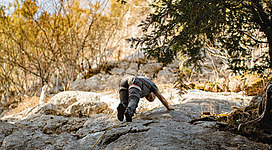 Klettergarten Kleefeld in Strobl: Das Bild zeigt eine Person, die eine schwierige Bergkletterroute überwindet. Die Umgebung ist von üppigen Wäldern und felsigen Gebirgszügen geprägt, was eine herausfordernde, aber auch malerische Landschaft ergibt.
