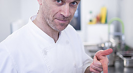 BIOEISECK - rEISECKERs Eismanufaktur in Regau: Ein Mann in weißer Kochkleidung mit buntem Kopftuch steht in einer Küche und hält eine Dokumentenmappe in den Händen. Er schaut konzentriert auf die Unterlagen.