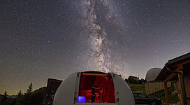 Ein Observatorium unter einem klaren Nachthimmel voller Sterne. Die Milchstraße ist deutlich sichtbar und das Observatorium strahlt rotes Licht aus.