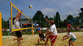 Beach-Volleyballplatz in Schärding: Eine Gruppe von Menschen spielt Volleyball auf einem Sandplatz. Es gibt ein gelbes Volleyball-Netz und verschiedene Personen in bunter Sportbekleidung, die den Ball über das Netz spielen.