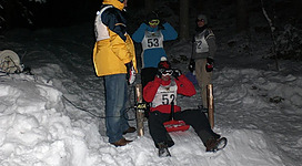Eine Gruppe von Leuten bereitet sich auf ein Schlittenrennen im Schnee vor. Es ist dunkel und die Teilnehmer tragen winterliche Kleidung.