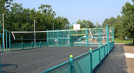 Funcourt in Weyregg am Attersee in Weyregg am Attersee: Das Bild zeigt einen öffentlichen Sportplatz mit einem Basketballkorb und einem umzäunten Spielfeld. Der Boden ist mit dunklem Asphalt belegt, und die Umzäunung sowie die Torbogen sind in einer hellen, grün-blauen Farbe gehalten. Die Umgebung ist von Bäumen und Vegetation umgeben, was eine angenehme, natürliche Atmosphäre vermittelt.