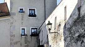 Stadtbefestigung Enns in Enns: Ein mehrstöckiges Gebäude mit einem Satteldach und mehreren Fenstern. Die Fassade ist teilweise verwittert, aber die Fenster wirken gepflegt. Eine Straßenlaterne erhellt den Durchgang zwischen den beiden Gebäuden. Insgesamt vermittelt das Bild den Eindruck einer älteren, traditionellen Architektur in einer ländlichen Umgebung.