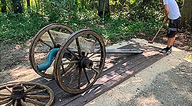 Wandergolfen am Weg der Vielfalt in Alkoven: Ein altes Wagenrad, das auf einem Waldpfad liegt. Eine Person in Freizeitkleidung ist dabei, die Räder zu betrachten.