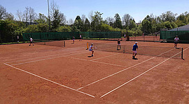 ATSV Schärding Tennis in Schärding: Eine Tennisanlage mit mehreren Tennisplätzen, auf denen Spieler aktiv sind. Die Plätze haben eine rötliche Lehmbahn-Oberfläche und sind von grünen Zäunen umgeben. In der Umgebung befinden sich Bäume und weitere Gebäude.