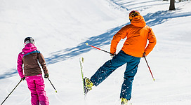 Zu sehen sind zwei Skifahrer von hinten, wie sie über eine präparierte Skipiste fahren.