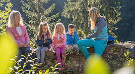 <p>Eine Gruppe von Kindern sitzt auf den Mauern der Ruine in der Natur. Zwei Erwachsene sind ebenfalls dabei und genießen die Zeit im Freien.</p>