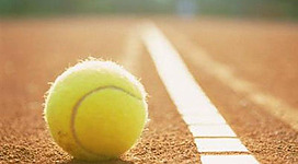 Ein Tennisball liegt auf einem Platz aus rotem Sand. Die Linie daneben verläuft in Richtung des Hintergrunds.