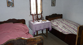 Freilichtmuseum "Brunnbauerhof" in Andorf: Ein Schlafzimmer in einem älteren, ländlichen Haus. Im Raum befinden sich ein großes Bett mit einer gemusterten Decke, ein kleiner Tisch mit Dekorationsgegenständen sowie weitere Möbel in traditionellem Stil. Das Zimmer wirkt gemütlich und nostalgisch.