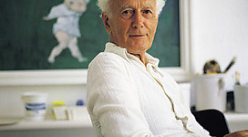 Fritz-Fröhlich-Sammlung in Wilhering: Ein erwachsener Mann mit weißen Haaren sitzt an einem Schreibtisch. Er scheint konzentriert und ernstfaft zu sein. Im Hintergrund ist eine Tafel zu sehen, auf der kleine Figuren zu erkennen sind.