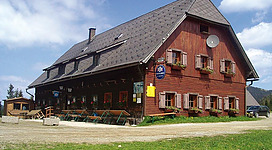 Ein traditionelles Holzhaus in ländlicher Umgebung. Die Fassade hat bunte Fensterläden und einen einladenden Außenbereich.