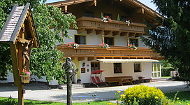Ein charmantes Ferienhaus mit Holzverzierungen und Blumen auf den Balkonen. Umgeben von einer grünen Wiese und Bäumen.