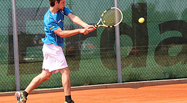 Ein Tennisspieler schlägt den Ball auf einem Sandplatz. Er trägt ein blaues Shirt und weiße Shorts.