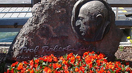 Robert Stolz Denkmal in St. Wolfgang im Salzkammergut: Das Bild zeigt eine Skulptur in Form eines Kopfes, die in einen Felsen eingelassen ist. Vor der Skulptur befinden sich rote Blumen, die den Blick auf die detailreiche Arbeit lenken.