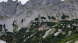 Eine beeindruckende Berglandschaft mit steilen Felsen und grünen Hügeln. Im Hintergrund ist ein kleines Gebäude zu sehen.