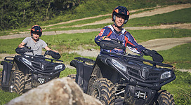 Zwei Männer die auf Quads auf einem Weg in einer Wiese fahren.