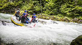 Ein aufregendes Rafting-Abenteuer auf einem Wildwasserfluss. Eine Gruppe von Personen paddelt in einem Schlauchboot durch sprudelnde Wellen.