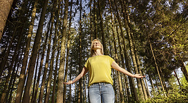 Foto SINNVIERTEL Tourismus_Johannes Kernmayer: Frau im Wald mit ausgebreitetten Armen und geschlossenen Augen genießt die Ruhe und die Natur