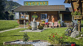 Ein stilvolles Schnapsbrennerei-Gebäude mit einem einladenden Garten. Zwei Personen stehen vor der Eingangstür und begrüßen die Besucher.