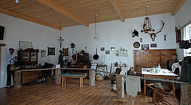 Ein historischer Raum mit Holzboden und einer Decke aus Holz. Es gibt verschiedene Möbelstücke, Jagdtrophäen und Ausstellungen an den Wänden.
