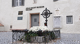 Ein weißes Gebäude mit dem Schild "Stille Nacht Museum Hallein". Vor dem Eingang befindet sich ein Blumenbeet mit einem Kreuz.