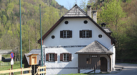 Ältester „Paarhofverband“ im Salzkammergut mit Wohnhaus, Stallstadel sowie angeschlossener Sägerei, Mühle, Gipsstampfe und Backstube. Ein kleines Museum in einem traditionellen weißen Haus mit Holzschindeldach. Fensterläden in dunklem Braun, dekorative Muster an den Wänden. Im Hintergrund grüne Hügel und Bäume, ein Weg führt am Gebäude vorbei.